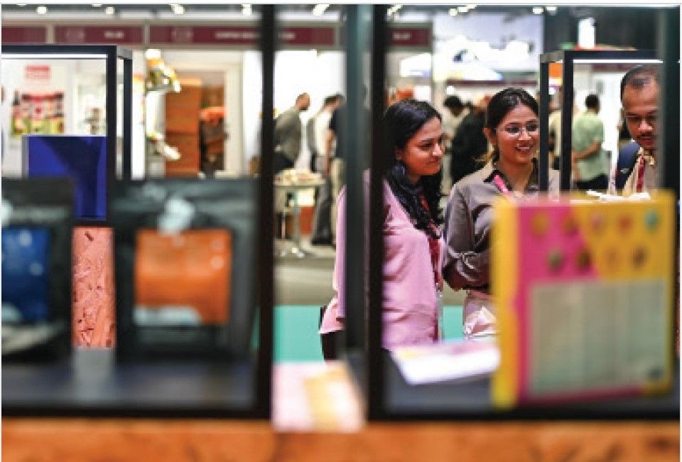 Three people standing at an exhibition booth, viewing the displayed items through glass frames.